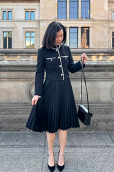 a lady wears a black tweed jacket and black pleated midi dress